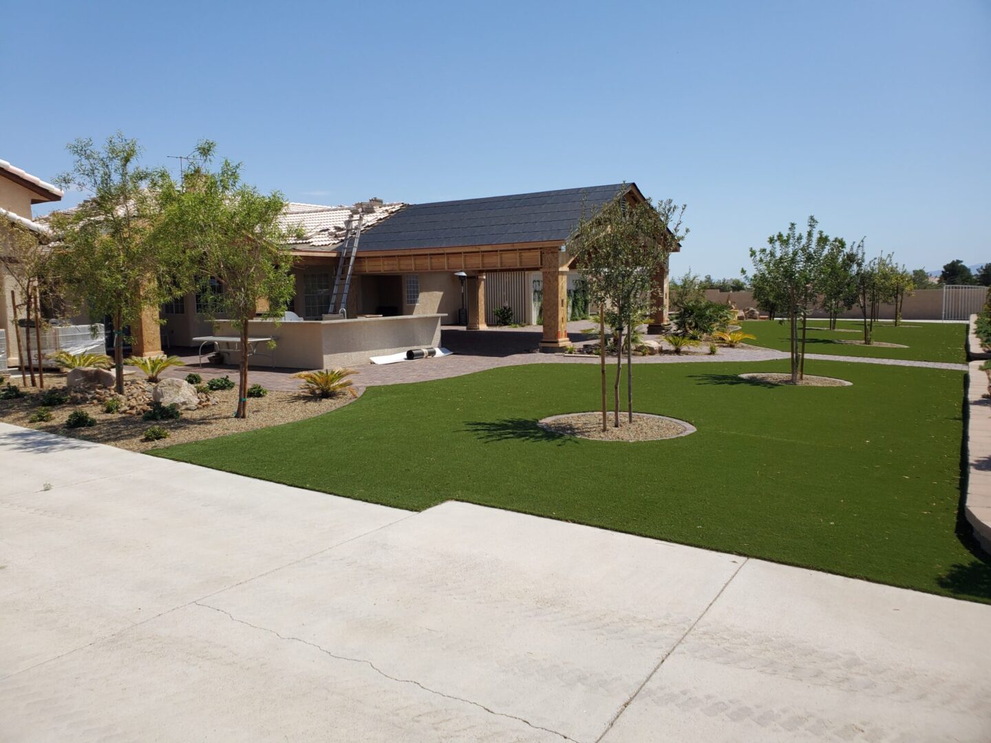 Spacious backyard with artificial turf, trees, and a covered patio.