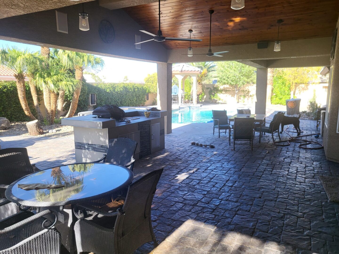Cozy outdoor patio with dining tables and a pool view under a wooden roof.