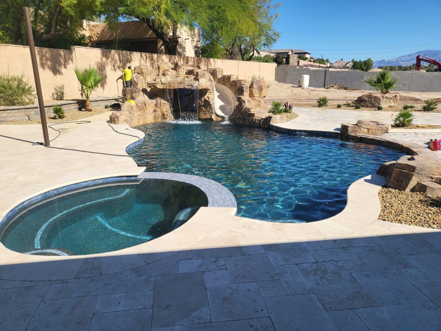 A backyard pool with a built-in hot tub and rock features under clear blue skies.