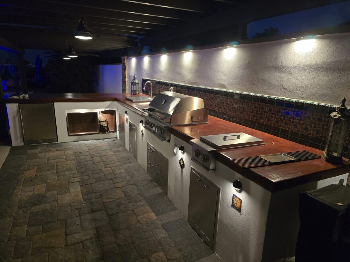 Modern outdoor kitchen setup with stainless steel appliances and stone countertops.