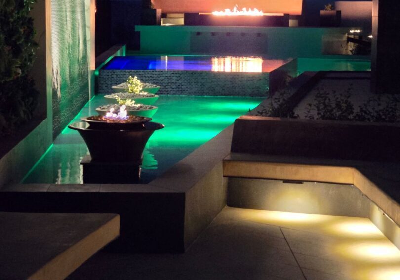 A beautifully lit outdoor pool area at night with cozy seating.